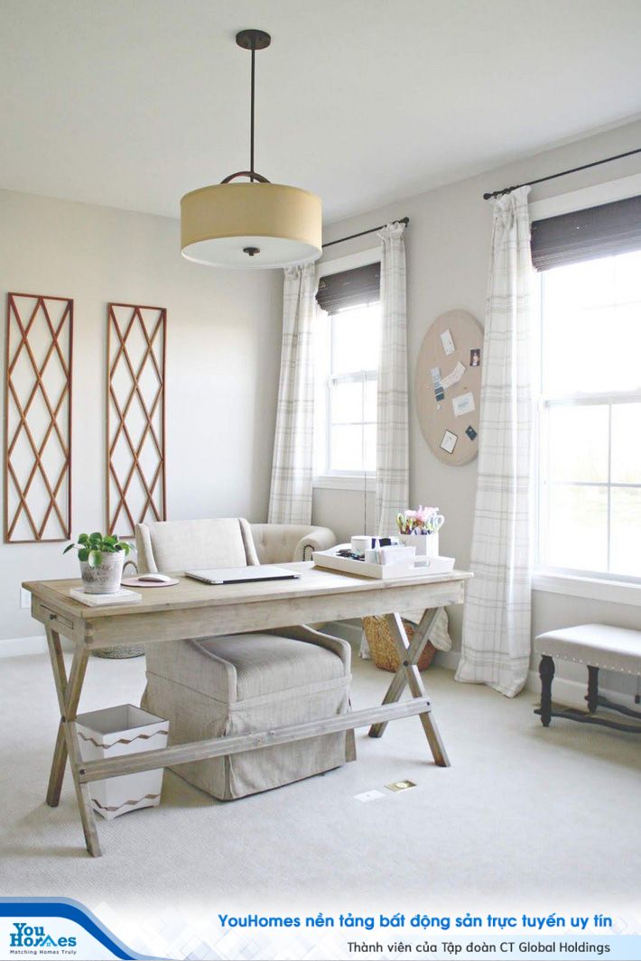 Một phòng làm việc tại nhà có màu trung tính với chất liệu gỗ trắng, nhiều hình in và luồng ánh sáng tự nhiên mạnh chiếu vào từ các cửa sổ.